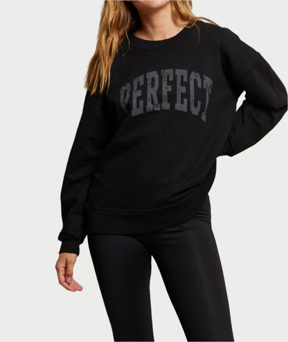 A woman wears an oversized black PERFECT Sweatshirt from perfectwhitetee, paired stylishly with black leggings. Her long blonde hair contrasts beautifully against the plain white backdrop, exuding a casual yet chic vibe.