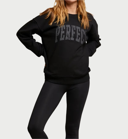 A person in an oversized black PERFECT Sweatshirt by perfectwhitetee, paired with black leggings, stands confidently with hands on hips against a plain background.