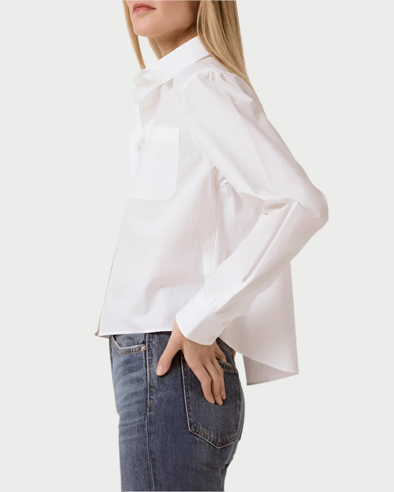 Against a light gray background, a person stands sideways in blue jeans, wearing the slightly oversized Coco Cropped Shirt by T. Line. This chic design features a chest pocket and is made from 100% cotton, effortlessly untucked for style.