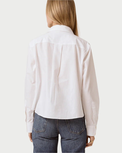 A person with long blonde hair is seen from the back wearing a T. Line Coco Cropped Shirt, made of 100% cotton, featuring long sleeves and a chic chest pocket, along with classic-fit blue jeans against a plain white background.