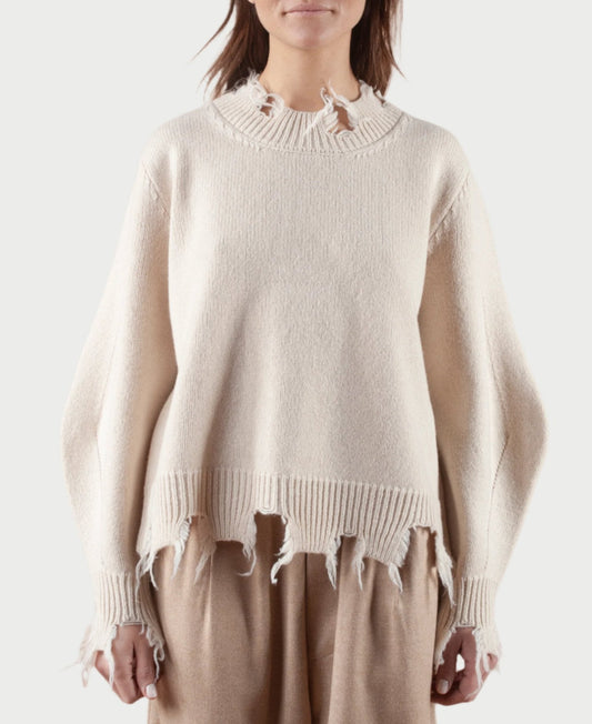 A person wearing the Turnable Sweater w/Banana Sleeves from Phisique du role, paired with light brown pants, stands against a plain background. The beige sweater showcases a distressed hem and cuffs, though the person's face is not visible.