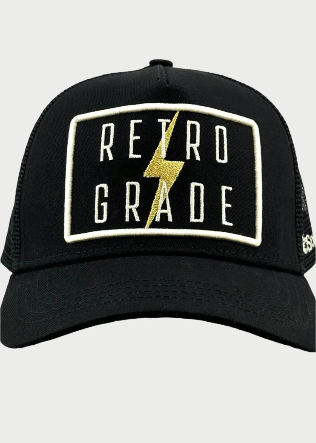 The Retrograde Trucker Hat by Soulbyrd is a black cap showcasing white embroidered text "RETRO GRADE" pierced by a yellow lightning bolt on a rectangular patch on the front panel. The hat features a mesh back, perfectly blending modern style with a nod to the retrograde phenomenon.