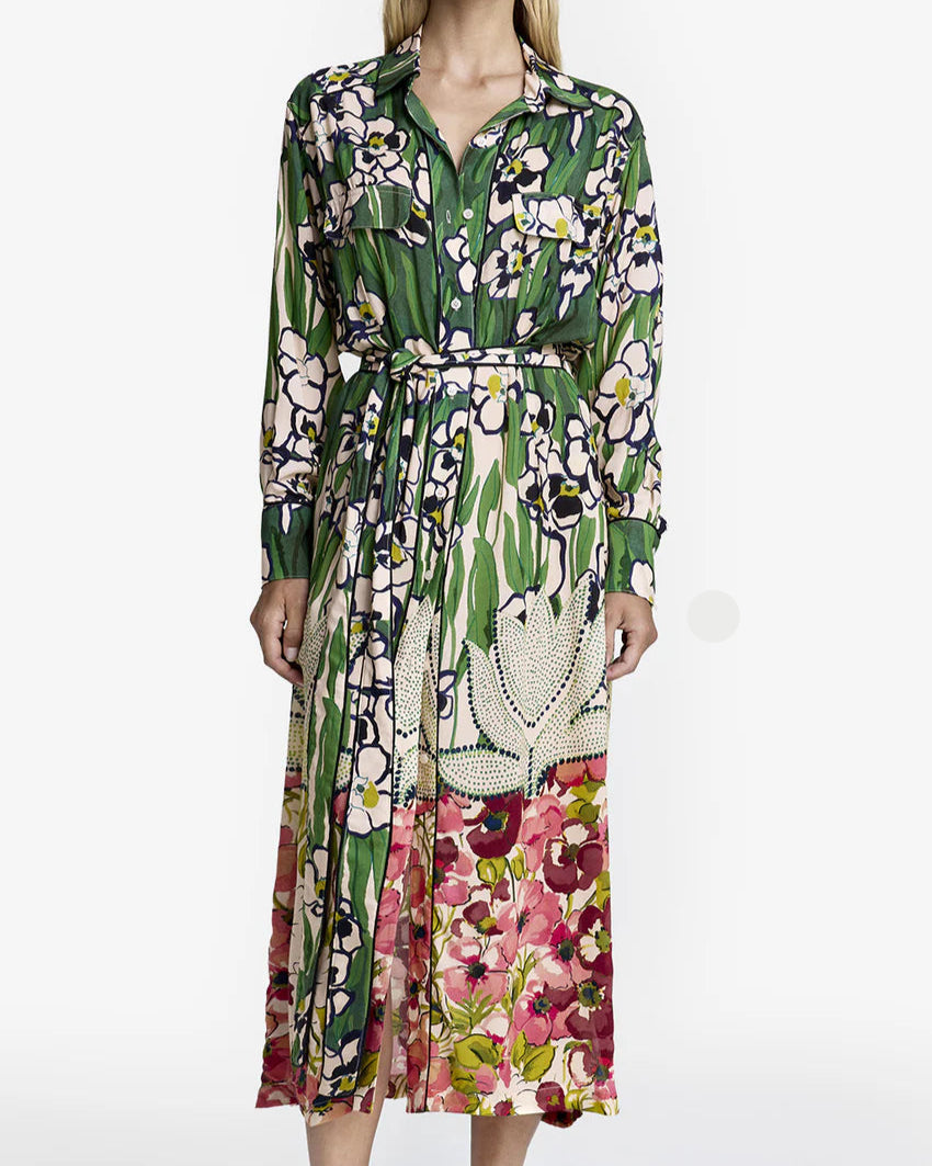 The person is wearing a Smythe Tailored Shirt Dress, Eco Vero-certified with a green, pink, and white floral garden print. It features long sleeves and a belted waist. They pair it with brown slippers against a plain white background.