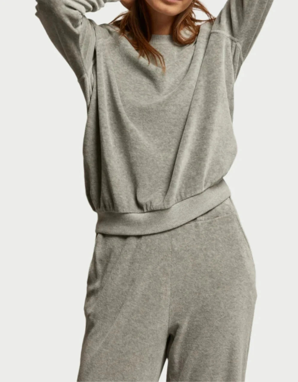 A person is dressed in a comfy, relaxed Stella Velour Sweatshirt from perfectwhitetee, paired with similar sweatpants, set against a simple backdrop. The photo captures the upper body while partially obscuring the face, emphasizing the luxurious shine of the velour material.