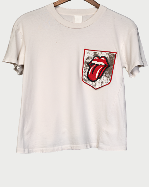 Madeworn's Rolling Stones Patch Pocket Tee features a distressed white design with a red tongue and lips graphic on the pocket, reminiscent of vintage rock t-shirts. This piece captures iconic Rolling Stones vibes for a classic style addition to your wardrobe.