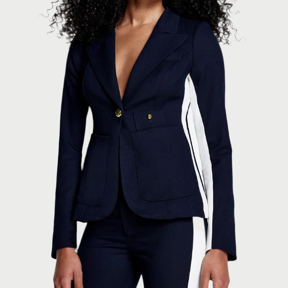 A person in a stylish Patch Pocket Stripe Blazer by Smythe, featuring navy stripes and gold buttons, paired with matching pants. The modern, fitted look perfectly complements their long, curly hair.