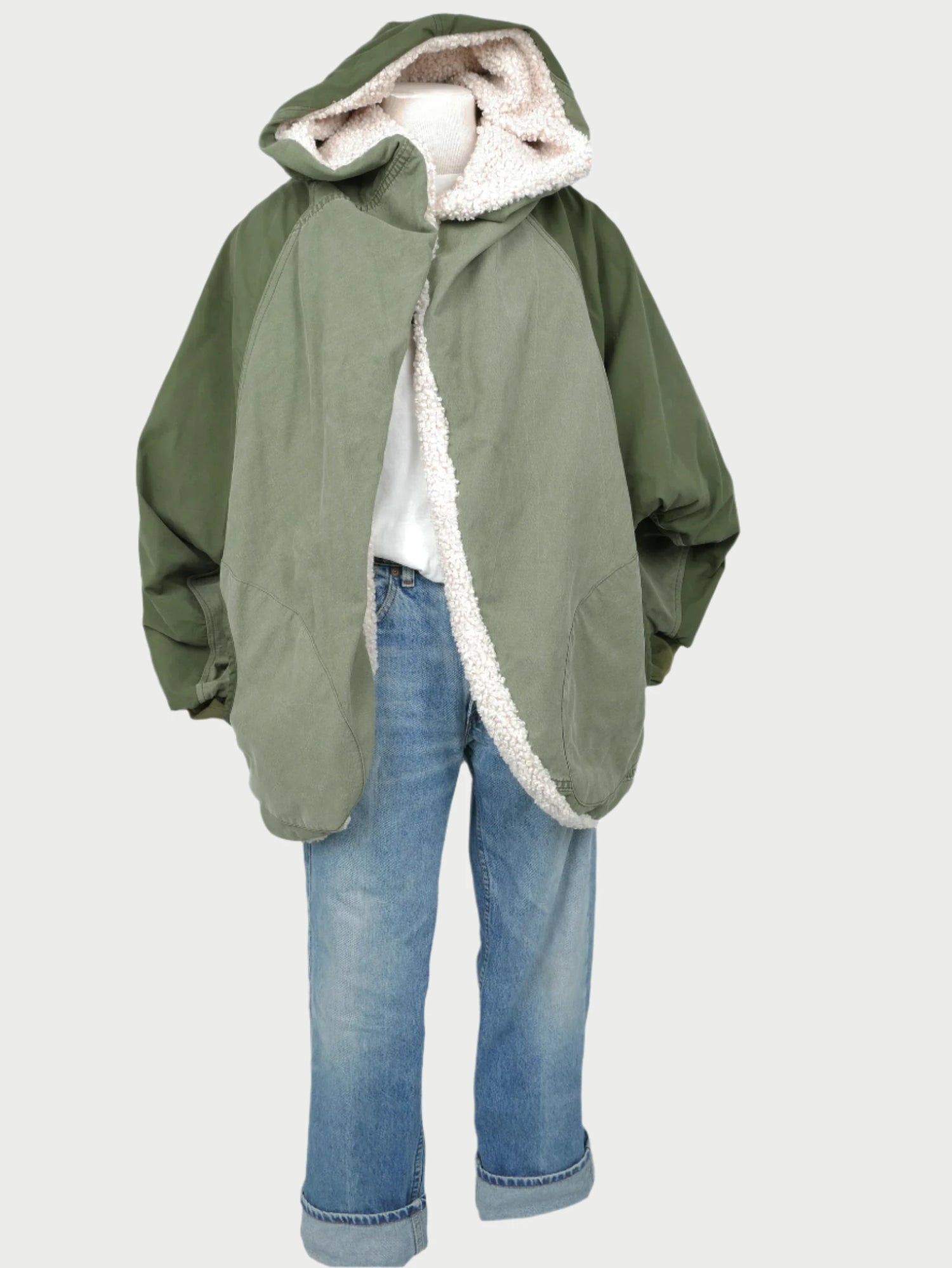 A children's ensemble includes a reversible Sherpa Bomber Jacket by SUPER READY, showcasing a green exterior and lined with soft white fleece. It's paired with a white shirt and blue jeans, which are stylishly rolled at the cuffs. This outfit is beautifully displayed against a plain background for an elegant presentation.