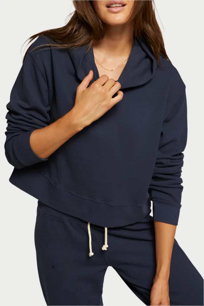 A person with long brown hair is wearing a dark blue French Terry Iggy Hoodie from perfectwhitetee, along with matching sweatpants. They are standing against a plain beige background, one hand adjusting the collar of the hoodie while the other rests by their side, looking directly into the camera.