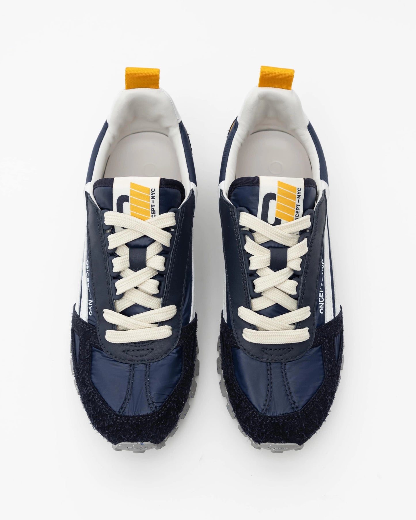 Introducing the Toronto Shoe by Oncept: a chic pair of navy blue sneakers featuring white laces and soles, accented with a yellow pull tab and a distinctive white logo on the tongue. These lightweight sneakers showcase a textured front and sporty design, perfectly presented against a white background.