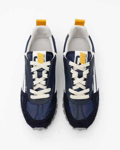 Introducing the Toronto Shoe by Oncept: a chic pair of navy blue sneakers featuring white laces and soles, accented with a yellow pull tab and a distinctive white logo on the tongue. These lightweight sneakers showcase a textured front and sporty design, perfectly presented against a white background.