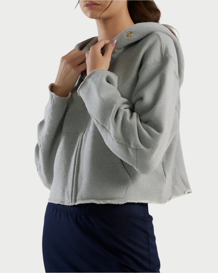 Wearing a Rosa Raw Zip Hoodie by Les Tien, the person in dark pants stands with hands near the hood. The image, set against a plain light background, is cropped just above the mouth.