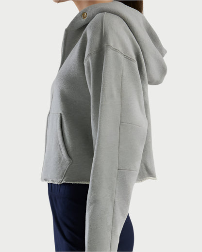 Side view of a person in a Les Tien Rosa Raw Zip Hoodie, crafted from soft cotton with a raw edge hem and front pocket. Paired with dark pants, the neutral background highlights the cozy aesthetic.