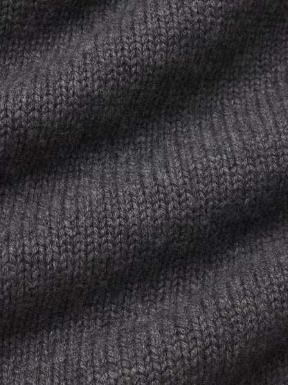 Close-up view of the dark gray knitted fabric from the Chunky V-neck Sweater by Frame, showcasing its intricate, tightly woven texture. The material appears soft and slightly ribbed, with a pattern of repeating, uniform stitches. The gentle folds suggest a luxurious blend in this oversized sweater, perfect for the cozy Fall season.