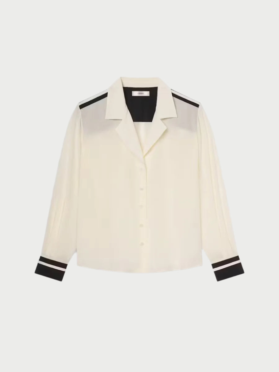 The Frame Silk Pajama Shirt is a white long-sleeve piece with black trim on the cuffs and shoulders. It features a notch collar, button-up front, black lining inside the collar, and offers a relaxed fit for versatile wear.