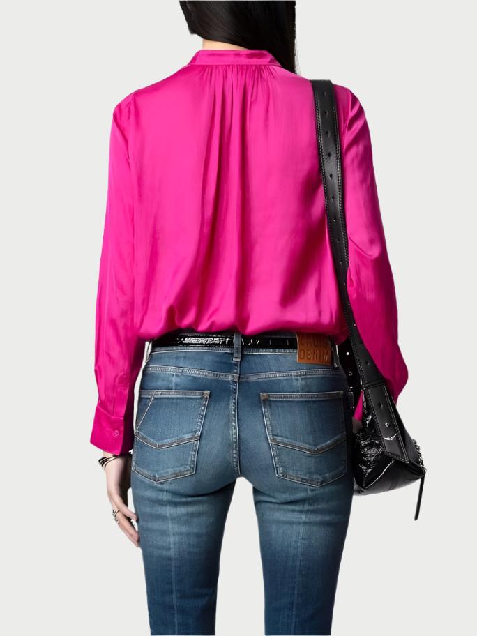 A person is wearing the Bright Pink Satin Blouse by Zadig & Voltaire and fitted blue jeans, standing with their back to the camera. They have a black leather shoulder bag adorned with studs.