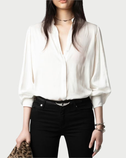 A person wears Zadig & Voltaire's Trenta Satin Blouse in white with puffed long sleeves and black pants, accessorized with a choker necklace and holding a leopard print bag, creating a chic ensemble against a plain, light-colored background.