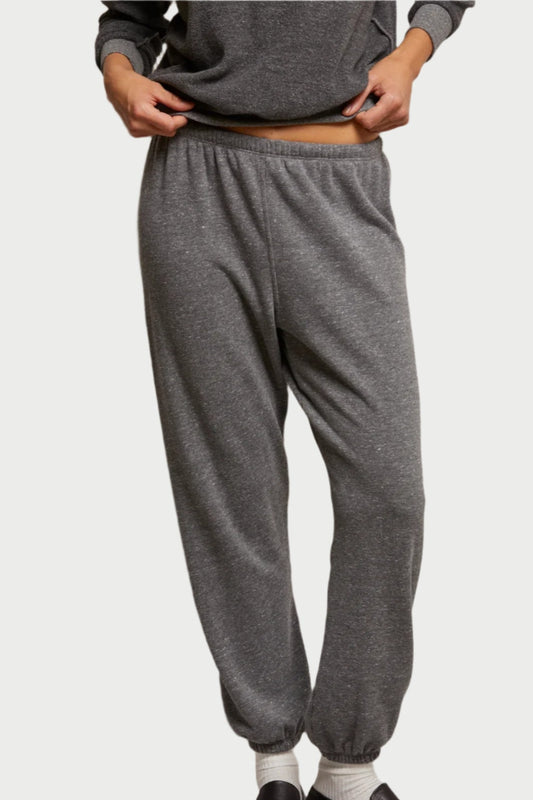 Against a plain background, a person adjusts their waistband, wearing perfectwhitetee's Stevie Sweatpants in Dark Heather Grey with a matching gray top and white socks.