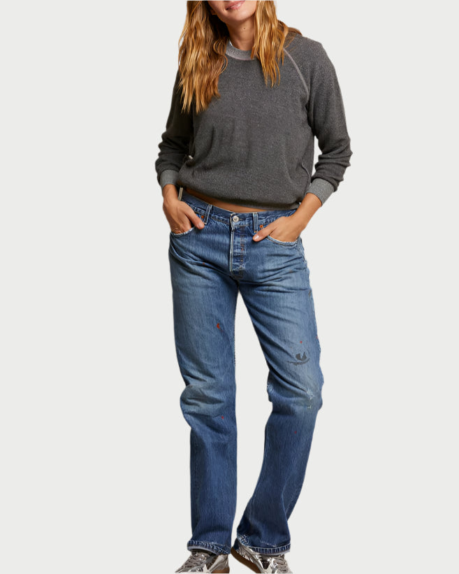 A person in a Ziggy Sweatshirt Dark Heather Grey by perfectwhitetee and blue distressed jeans with sneakers stands against a plain background. The jeans, featuring wear marks and exposed seams, add a casual touch. Their hands are in their pockets, exuding effortless style.