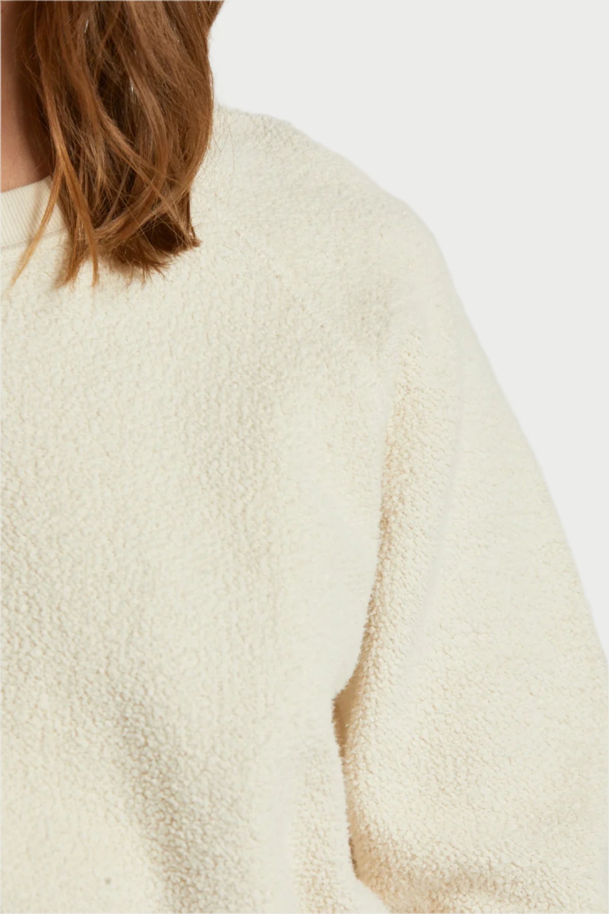 Close-up of a person wearing the Ziggy Bright Ivory sweater by perfectwhitetee, showcasing its textured design and exposed seam detailing on the shoulder and upper arm, with some hair visible against a neutral background.