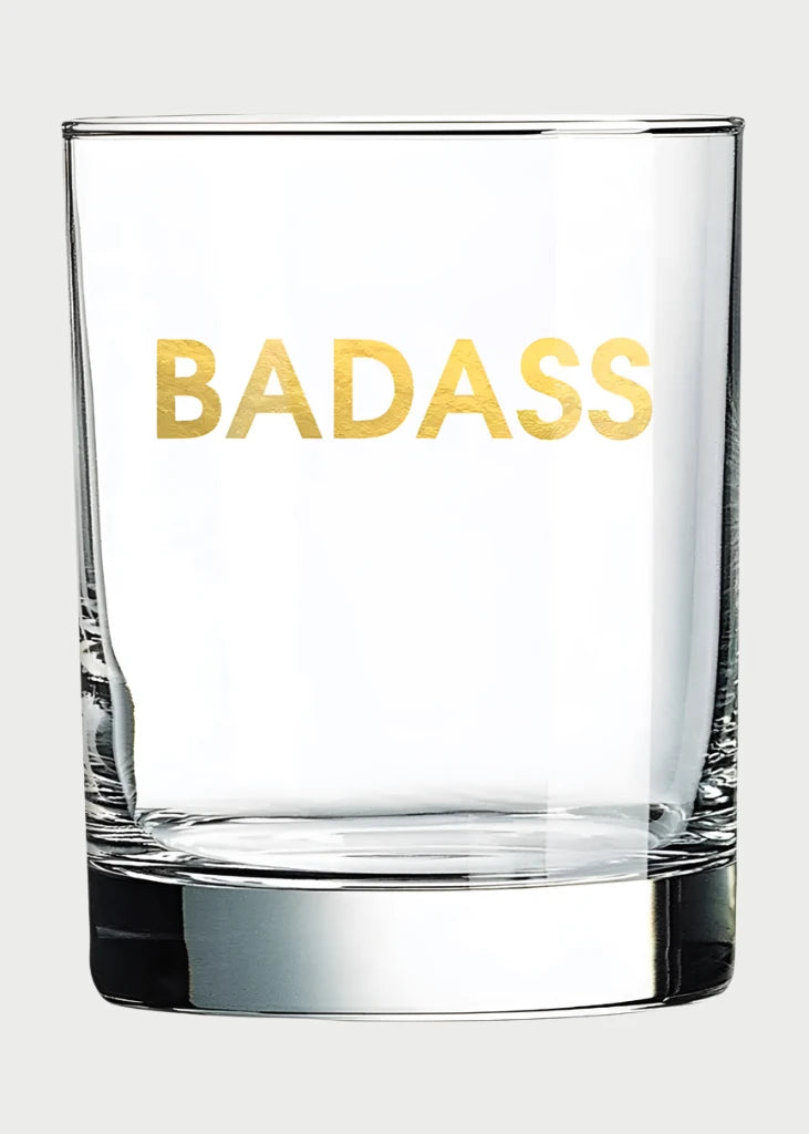 Chez Gagné's Rocks Glasses boast "BADASS" in bold gold foil on clear glass, creating a stylish contrast against a light backdrop—an ideal gift for those who value unique and daring designs.