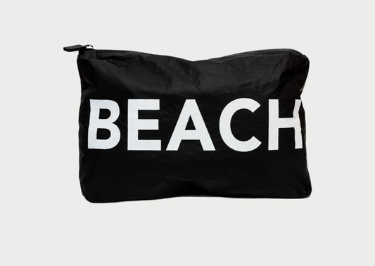 The Printed Pouch- Beach by LOCAL BEACH is a black water-resistant pouch made from 100% Tyvek fabric, featuring the word "BEACH" in large white letters on the front. Ideal for organizing travel toiletries, it stands out beautifully against a plain light gray background.