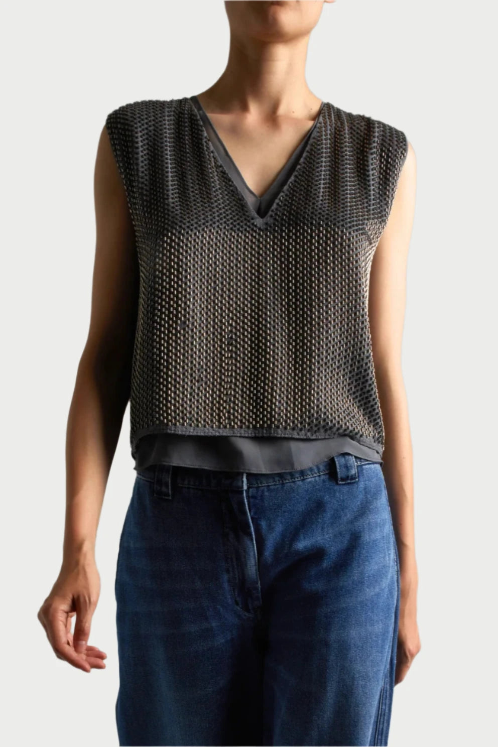 A person wearing the Cassidy Beaded Top by Saint Art NY, paired with loose-fitting blue jeans, walking forward on a light gray background. The individual’s head is cropped out of the frame.