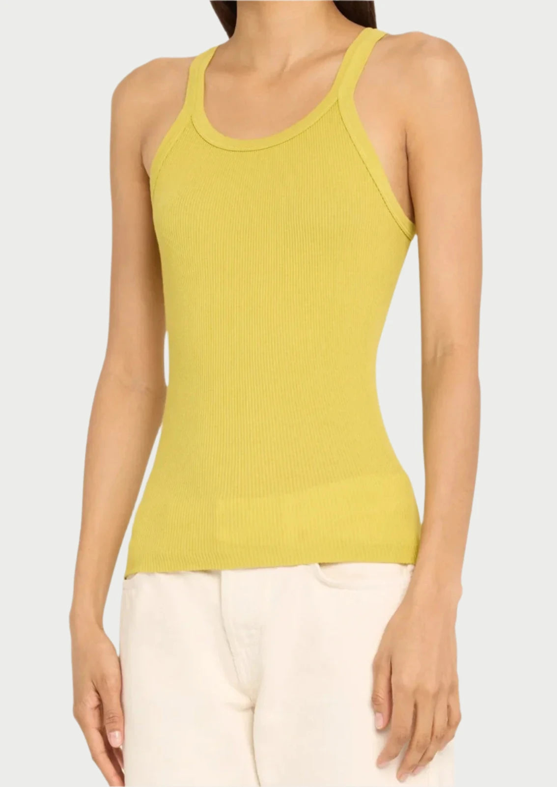 A person is wearing a sleeveless, yellow ribbed Pear Ribbed Tank by RE/DONE paired with white pants. They are standing against a white background. The basic tank top has a fitted design and a round neckline, capturing the essence of summer color. Only the upper body and waist down to the hips are visible.