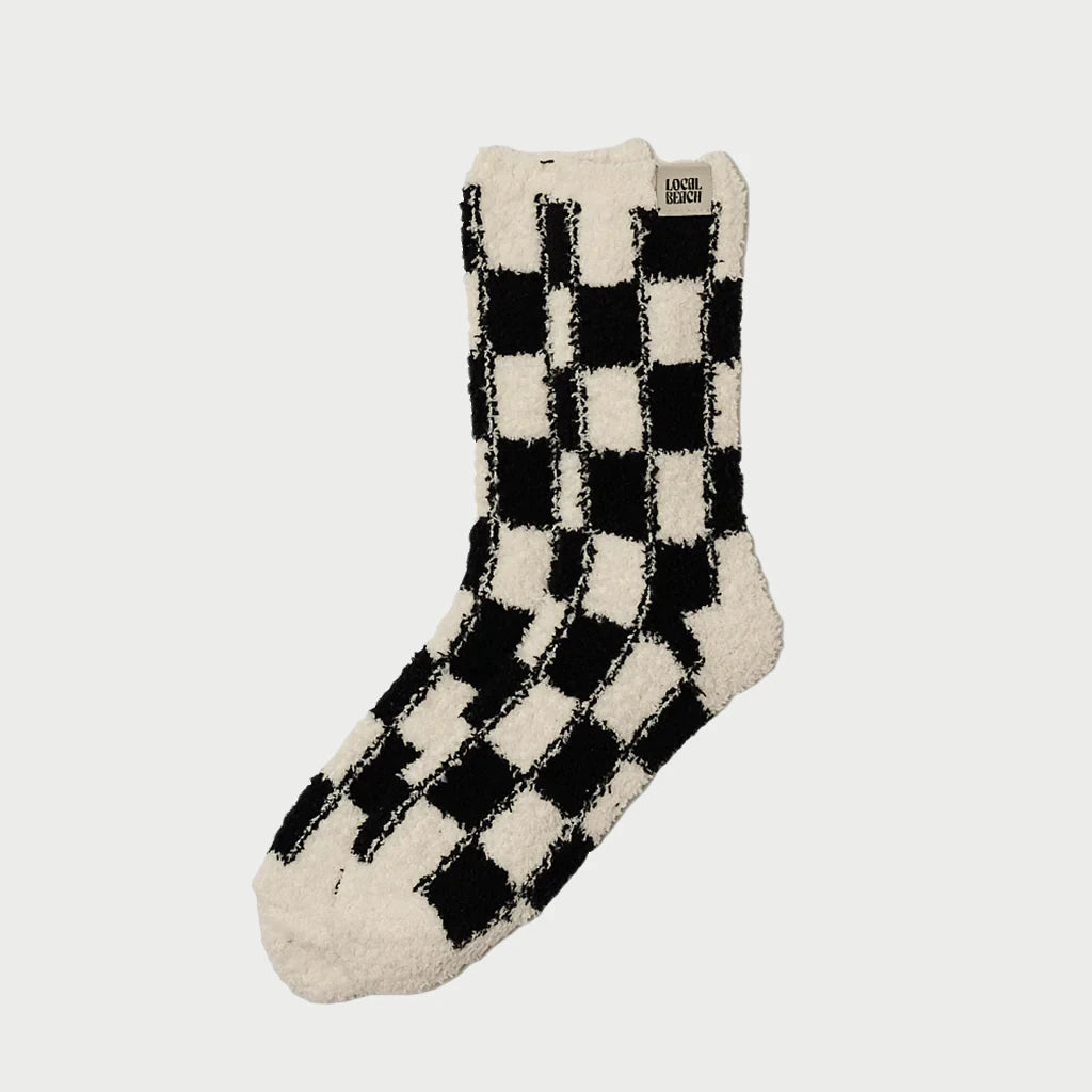 Explore the Cozy Socks collection from LOCAL BEACH with this black and white checkered fuzzy slipper sock, expertly crafted using Feather Knit technology. A small label on the cuff adds a charming detail, making it a perfect addition to your comfort essentials.