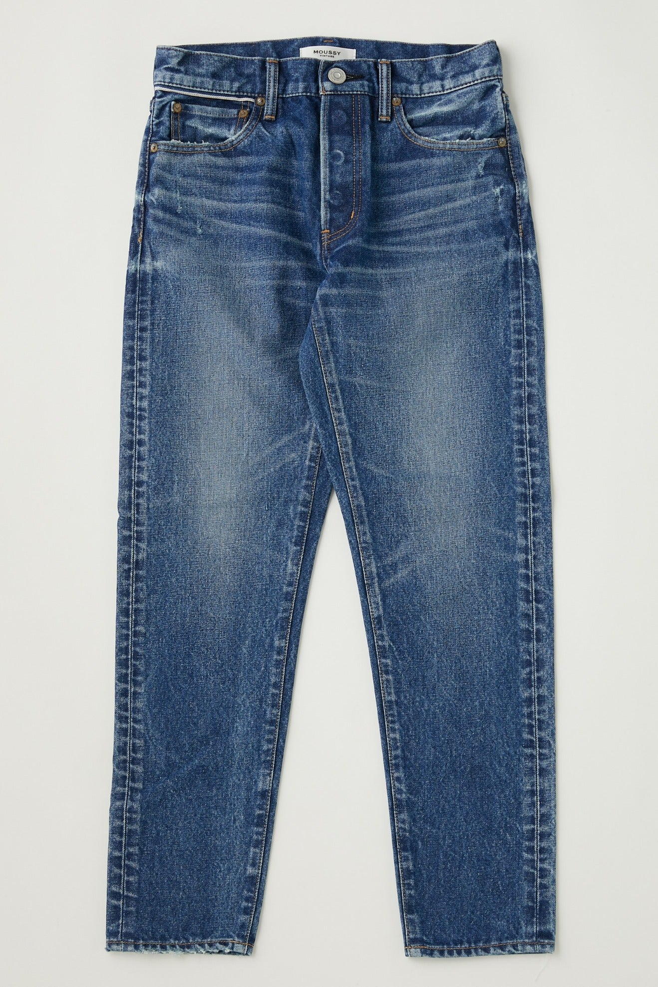 The Forestville Tapered Jeans by Moussy are mid-rise blue denim with a classic five-pocket design, slight fading, distressing, whiskering on the thighs, a straight leg cut, button and zip closure, and contrast stitching.