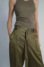 Load image into Gallery viewer, A person is pictured from the shoulders down, dressed in a sleeveless, ribbed tank top in an olive shade and Saint Art NY&#39;s high-waisted Charmeuse Pants, also in olive. The cargo-inspired Charmeuse Pant features a fabric belt with a metal ring buckle and zippered pockets. The person&#39;s hands rest in their pockets.