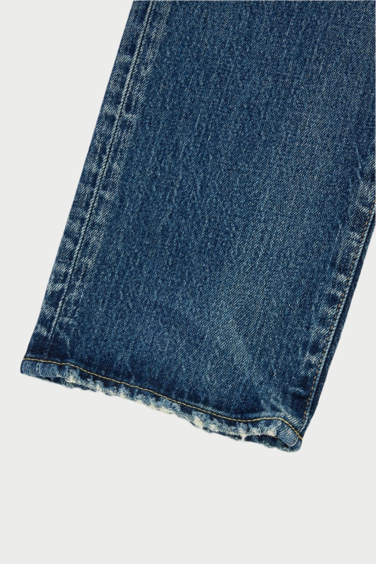 Close-up of a pair of dark blue mid-rise jeans highlighting the texture of the fabric. These Florahome Slim Straight Jeans by Moussy feature a frayed hem that lends them a slightly worn look. The visible detailed stitching along the seams showcases the craftsmanship of the heavy weight denim.