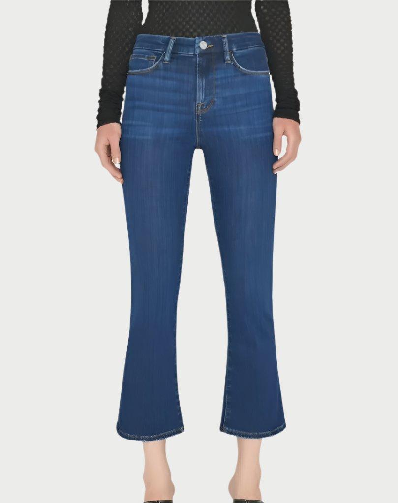 A person is styled in Frame's Le Crop Mini Boot Jeans in dark blue, made from a sustainable stretch cotton blend with a mid-rise waist. They are paired with a black long-sleeve top and black shoes, all set against a plain white background.