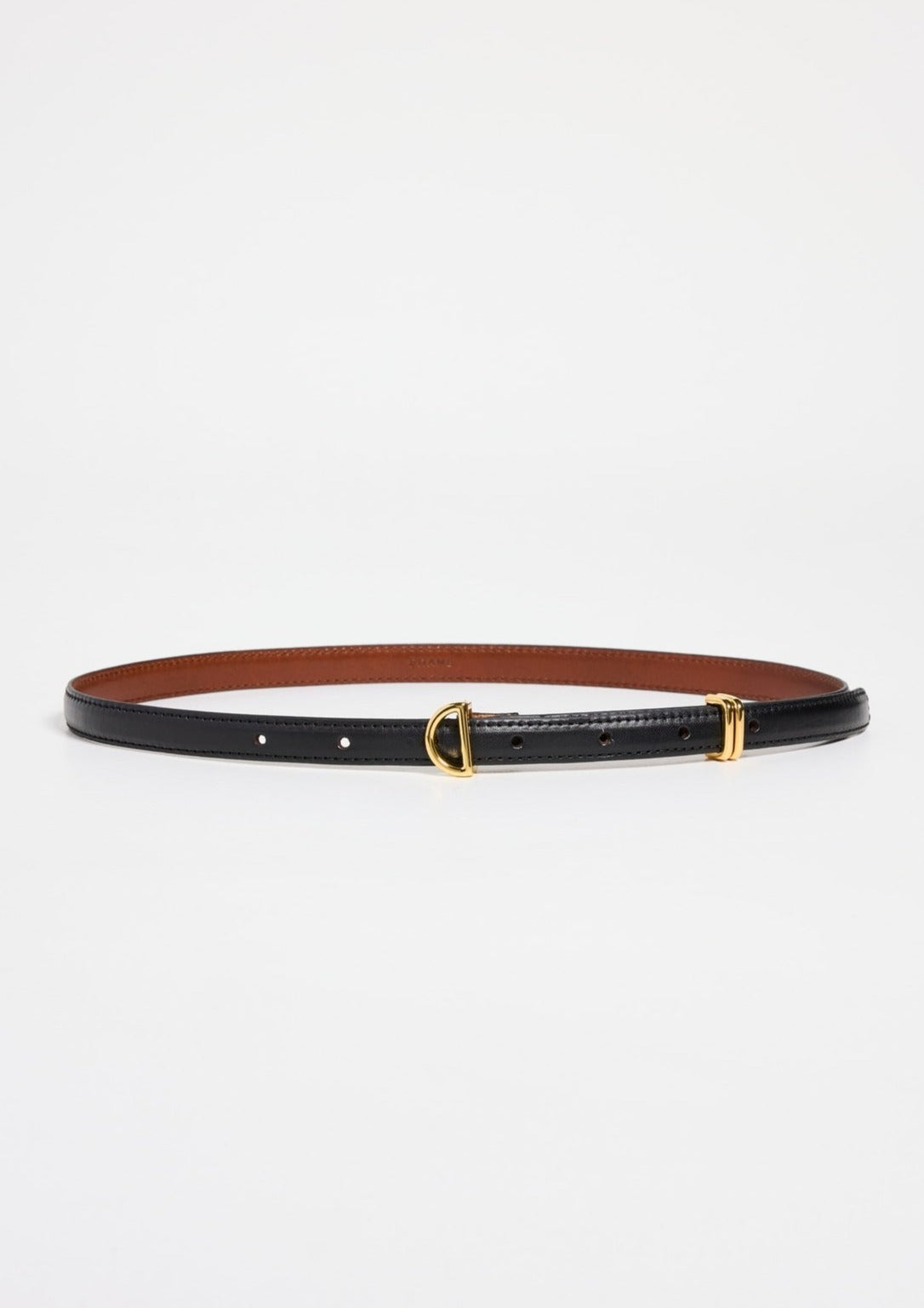 The Petit Crescent Belt by Frame, made from sleek black cowhide leather, boasts a small gold-tone buckle and a refined gold D-ring detail. The inner lining is brown. Laid flat against a white background, its understated elegance shines through.