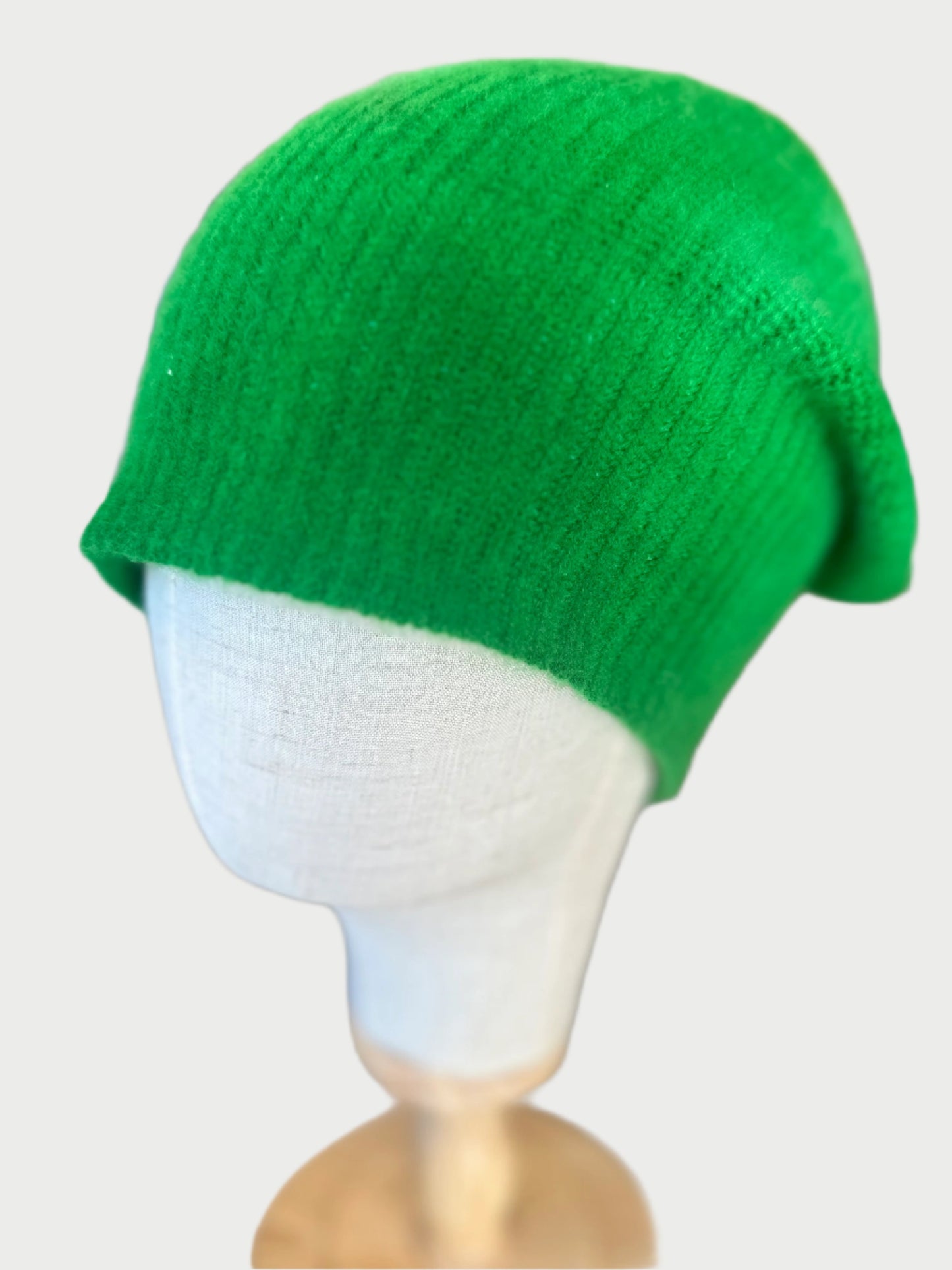 The MAREA Dip Dyed Beanie in bright green is showcased on a white mannequin head with a blurred background that highlights its texture and vibrant color, all enhanced through an artisanal dye process.