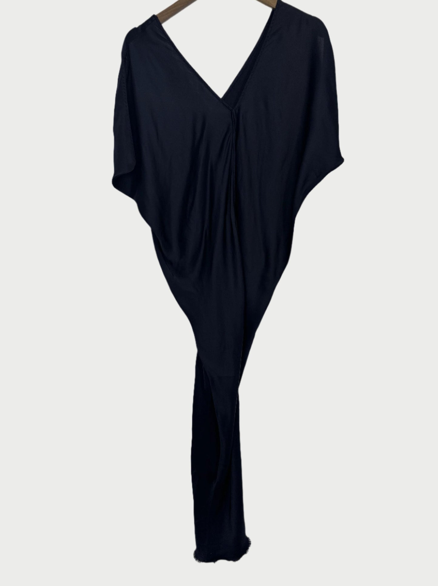 A Leah Dress by Jaga LA, featuring a black color, V-neck, and draped sleeves, is hanging. Made from travel-friendly, high-quality fabric, it appears soft and lightweight with a cascading silhouette.