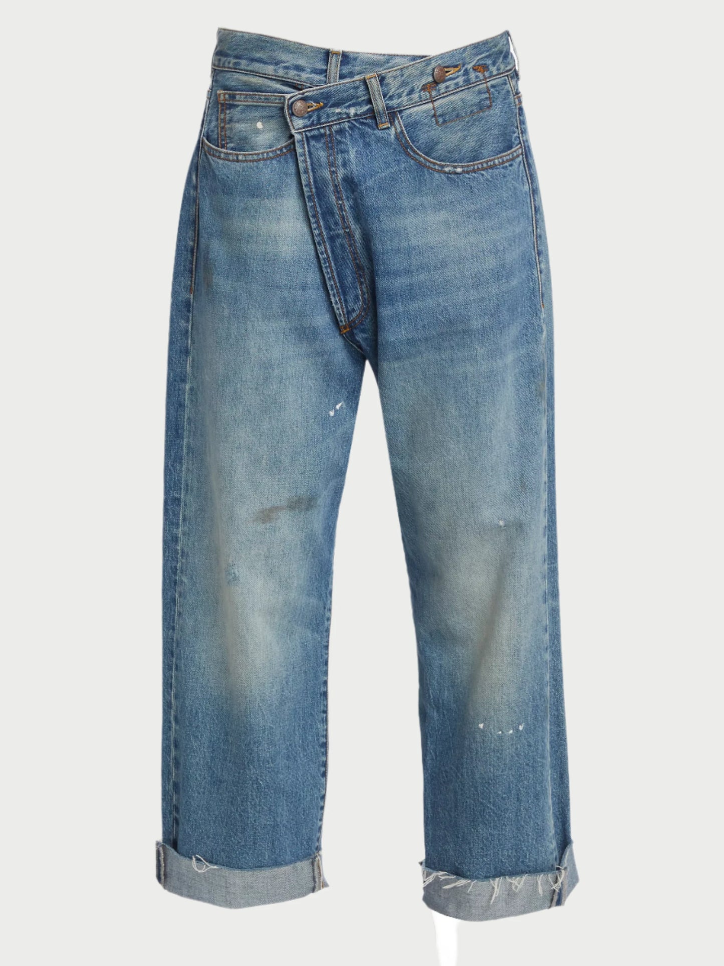 The R13 Crossover Jeans offer an industrial-inspired, distressed appearance with a unique design twist. Featuring rolled-up cuffs and an asymmetric waistband, these denim jeans showcase a faded texture and small paint splatters for added character.