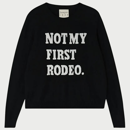 A cashmere crewneck sweater from JUMPER, featuring long sleeves, black fabric with white text on the front that reads "NOT MY FIRST RODEO," and a tag near the collar that says "jumper 1 2 3 4.