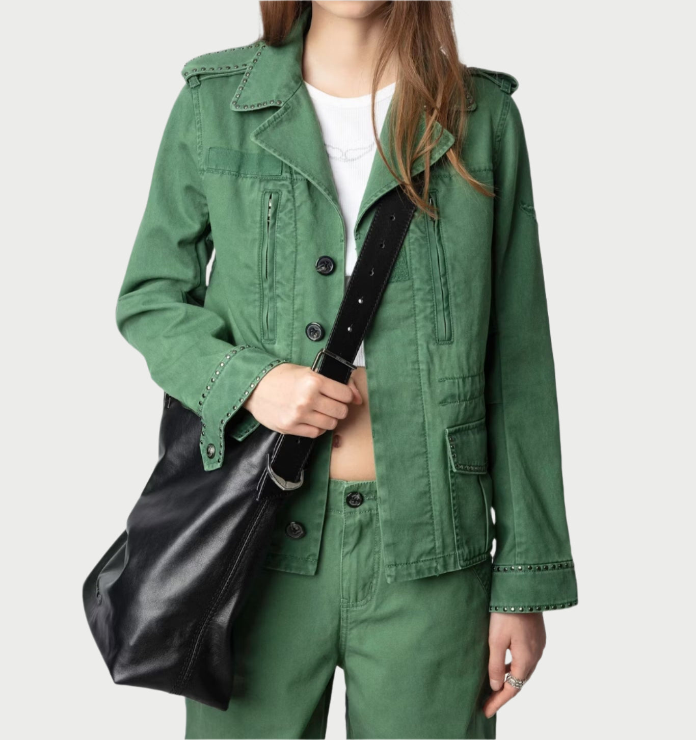 A person dons a Zadig & Voltaire Klimi Utility Jacket with matching pants, carrying a large black leather bag over their shoulder. The white shirt beneath the military-inspired jacket peeks out against a light gray background.