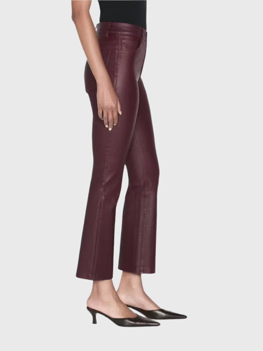 A person is wearing the Le Crop Mini Boot Leather Pants by Frame in burgundy lambskin stretch leather, paired with black pointed-toe heels. They stand sideways against a white background, highlighting the fit and style of these pants, ideal for fall fashion.