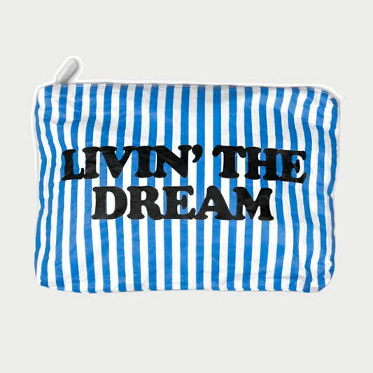 Introducing the Printed Pouch - Livin' The Dream by LOCAL BEACH: a travel toiletries organizer with a sleek design featuring blue and white vertical stripes, a top zipper, and made from water-resistant Tyvek fabric. It prominently displays the bold phrase "LIVIN' THE DREAM" across the front.