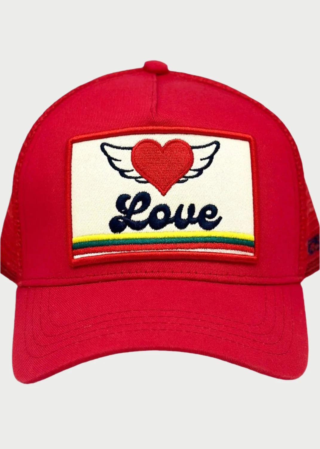 The Love Wings Trucker Hat by Soulbyrd is a red baseball cap featuring an embroidered patch on the front. The patch displays a red heart with white wings above the word "Love" in black cursive text, with a rainbow stripe running across the bottom, embodying the joyful spirit of Soulbyrd's LOVE WINGS collection.