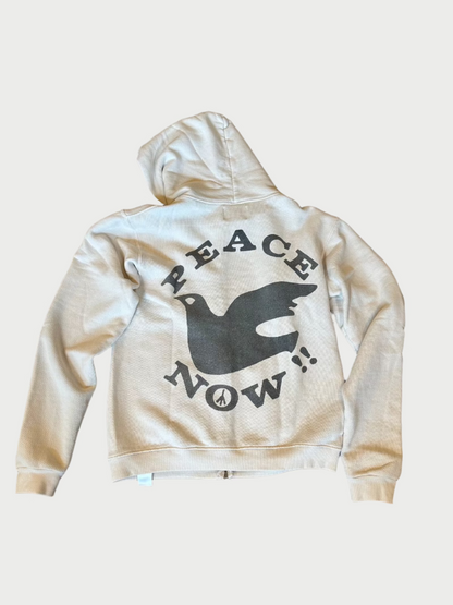 A white, Madeworn Peace Now Hoodie is laid flat on a wooden floor. The back of this vintage-inspired design features a large, black graphic of a dove and the text "PEACE NOW!!" in bold letters, with a small peace symbol below the dove.