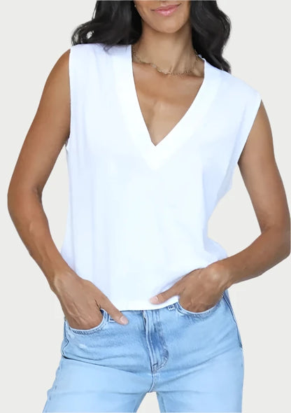 A person wearing a Margot V Neck Sleeveless Tee by perfectwhitetee and light blue jeans is standing against a plain background, their hands casually tucked in their pockets.