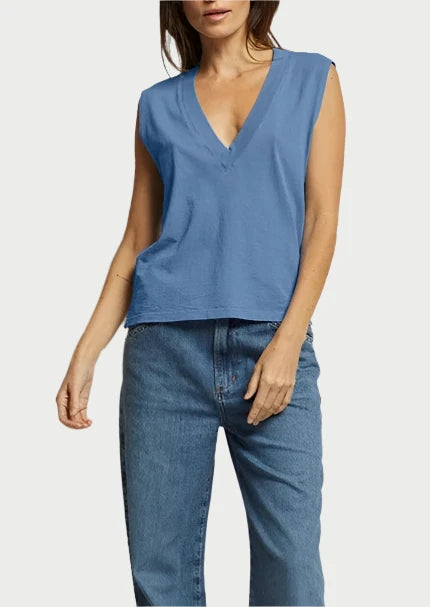 A person wearing the Margot V Neck Sleeveless Tee in Carolina Blue from perfectwhitetee and blue jeans stands against a plain white background. Their right arm is relaxed by their side, and their left hand is tucked into their jeans pocket. The outfit, made from signature cotton fabric, creates a flattering silhouette even with their face partially out of view.