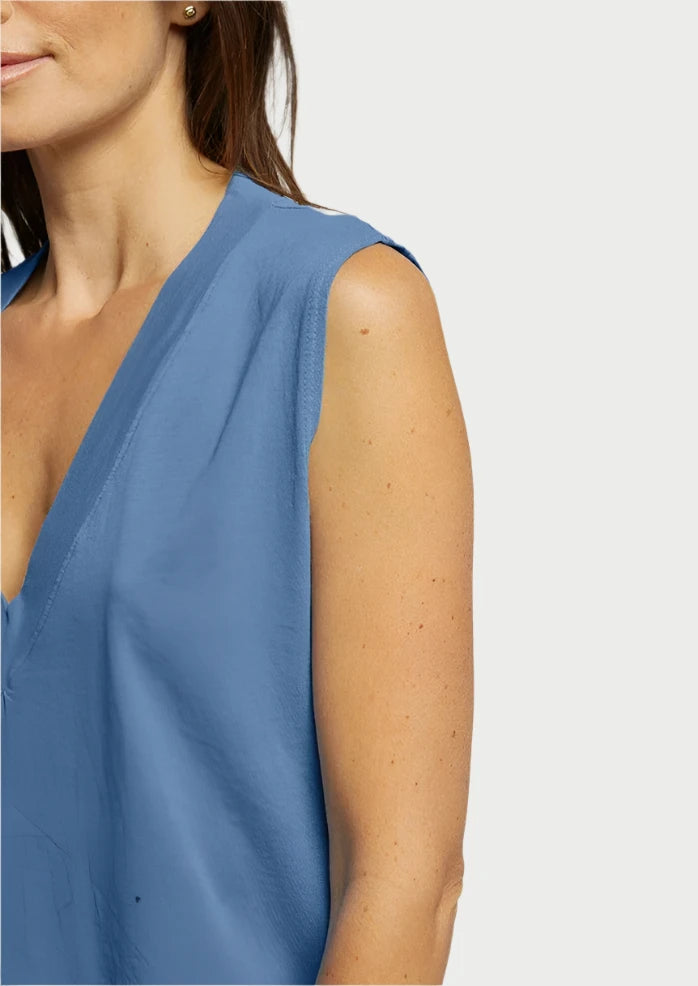 Partial view of a woman in a Margot V Neck Sleeveless Tee - Carolina Blue by perfectwhitetee, creating a flattering silhouette. Only the right side of her upper body and her right arm are visible. The background is plain and light-colored. Her brown hair falls loosely over her shoulder, highlighting the effortless charm of this signature cotton fabric piece.