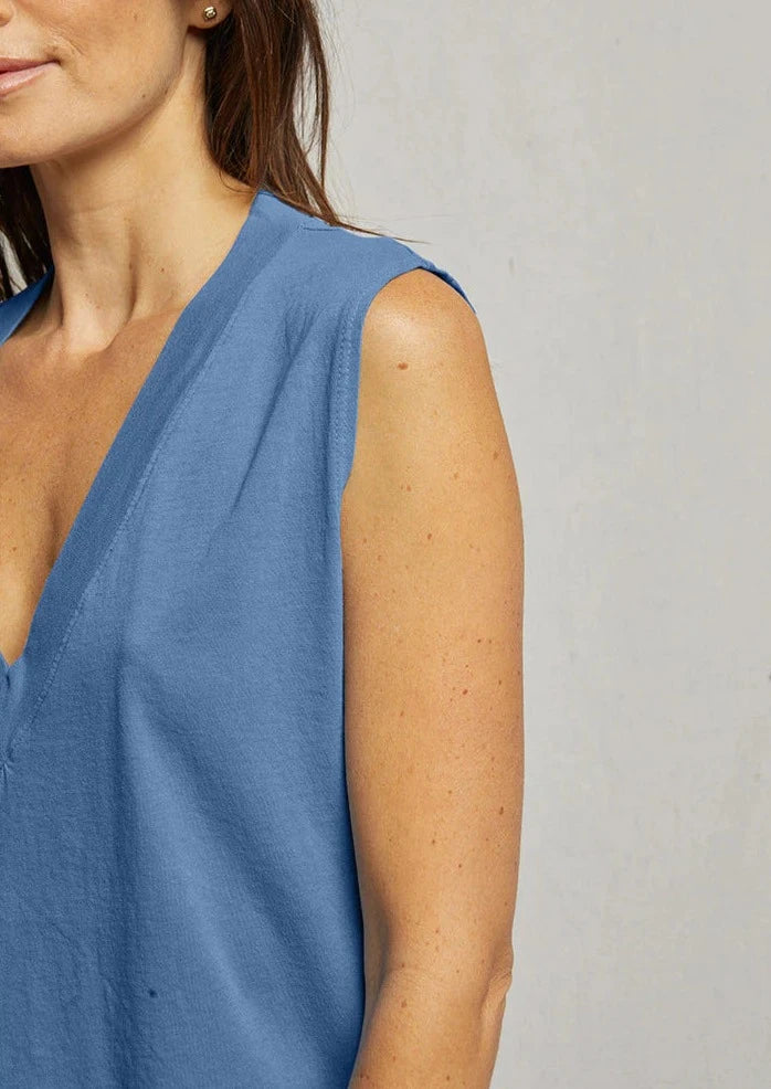 Close-up of a person wearing a sleeveless V-neck blue top, Margot - Carolina Blue by perfectwhitetee, made from signature cotton fabric for a comfortable fit. The person is shown from the shoulders to the midsection, with their face partially out of the frame. The background is a plain light gray wall.