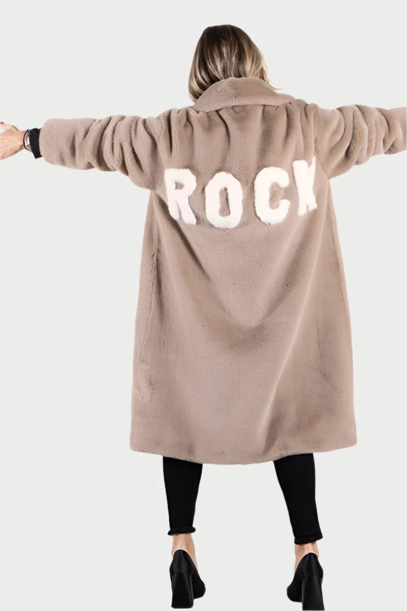 A person with arms outstretched facing away from the camera is wearing the "Mr Greys Rock Coat" by ANGEL WINGS, a long, light brown faux fur jacket featuring the word "ROCK" in large white letters on the back. They are also wearing black pants and black boots against a plain white background.