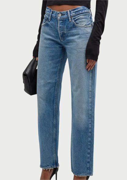 A person dressed in Cheval Straight-Low Jeans by Moussy, featuring a light wash with a subtle fade and frayed hems. They pair the jeans with a black long-sleeve top and carry a black purse. The image focuses on the lower half of their stylish outfit, highlighting their chic look.