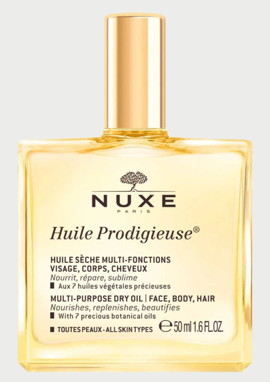 A square-shaped bottle of NUXE Huile Prodigieuse Travel Size, a multi-purpose dry oil with natural ingredients for face, body, and hair. The clear bottle with a gold cap contains 50 ml (1.6 fl oz). The label highlights its dry oil texture that nourishes, repairs, and beautifies all skin types.