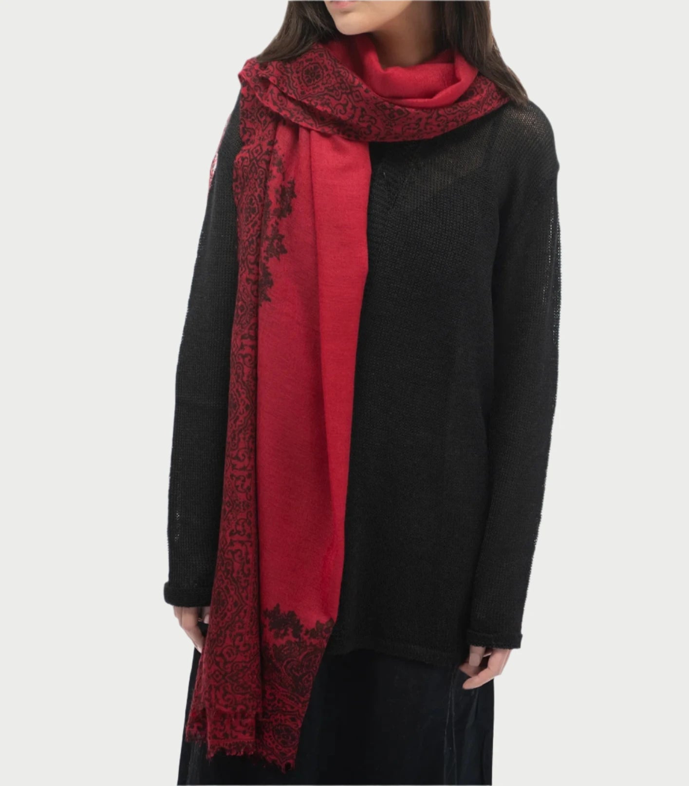 A person wearing a black sweater and a 100% cashmere scarf adorned with intricate Paisley designs is shown from the shoulders down. The Whisperweight Paisley Scarf by Meg Cohen, elegantly draped over one shoulder, complements their long hair against the plain white background.